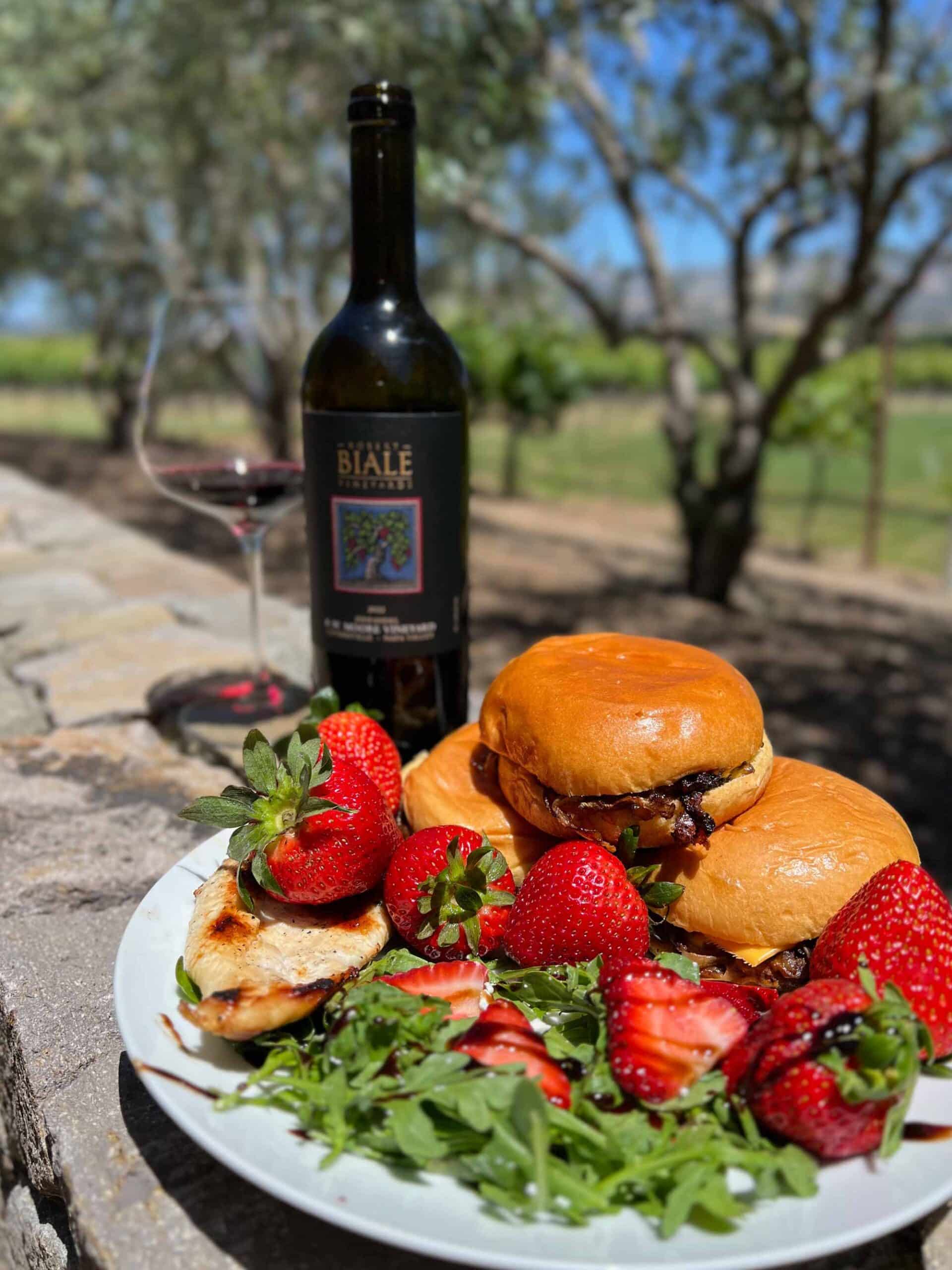 plate of arugula salad with strawberries and a burger, set beside a bottle and glass of Biale's RW Moore Zinfandel