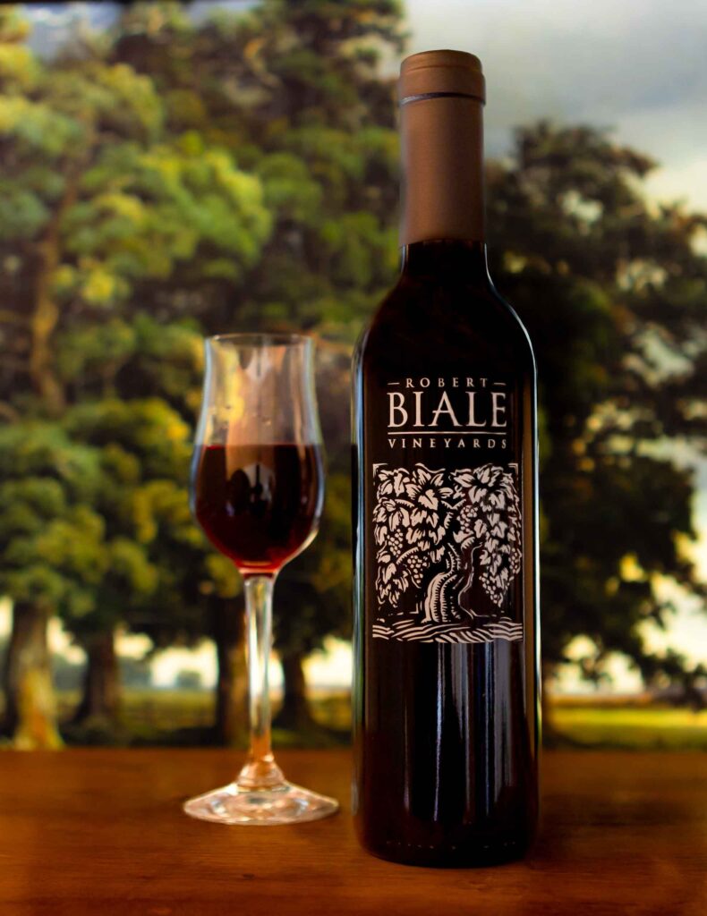 bottle of Biale Petite Sirah dessert wine beside a filled port glass on a wooden table