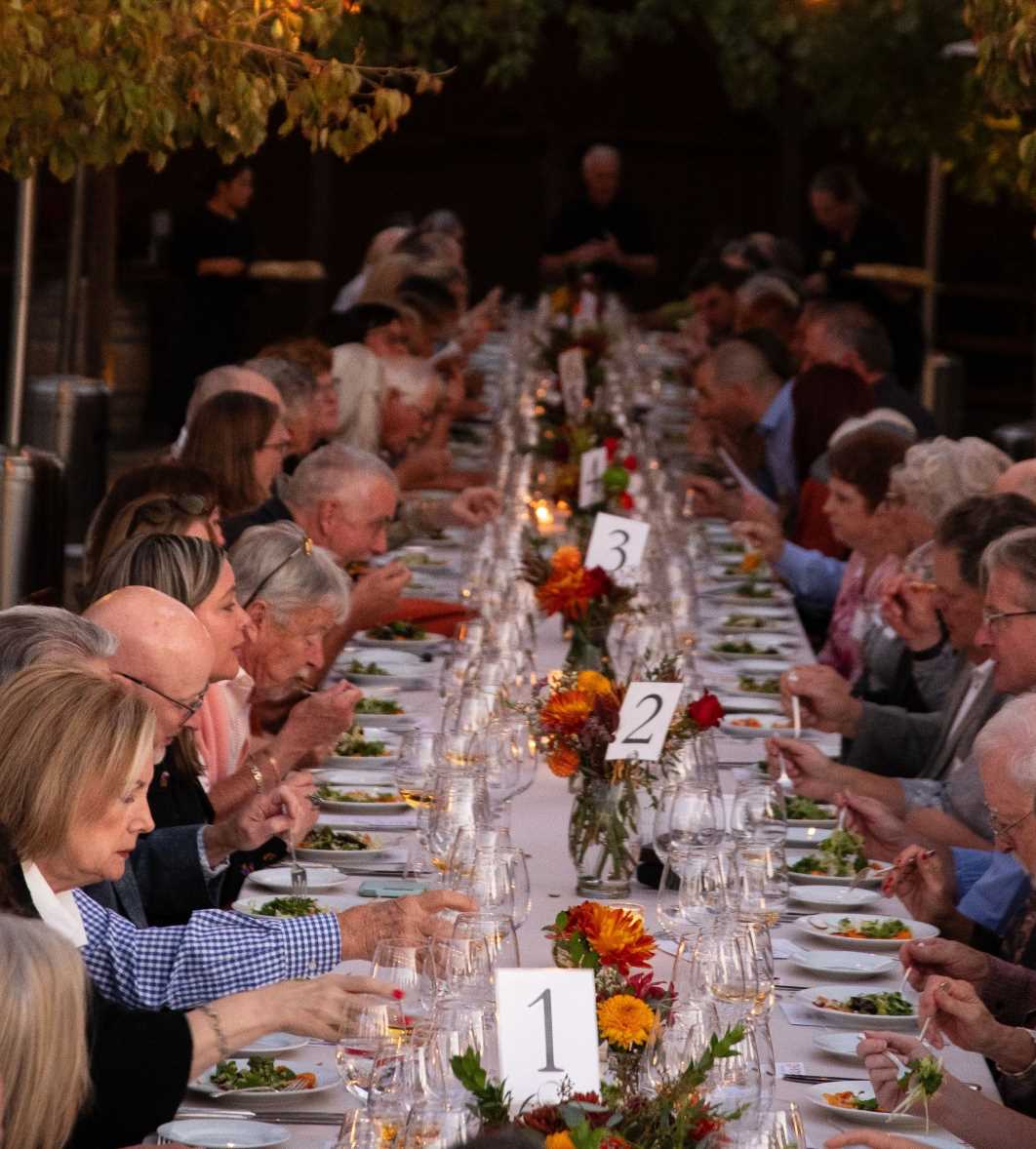 looking down a long dinig table with diners on either side and a row of vases of flowers down the middle